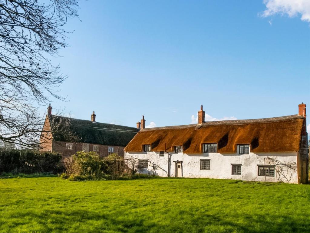 an old house with a thatched roof on a green field at Ashford Old Farm in Ilton