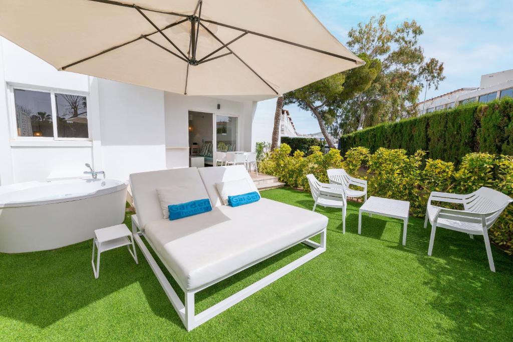 een patio met een parasol en stoelen en een bad bij Palm Garden in Port d'Alcudia