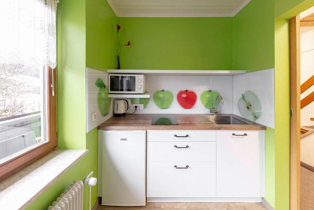 una pequeña cocina con paredes verdes y armarios blancos en Apartments Kot'č en Kranjska Gora