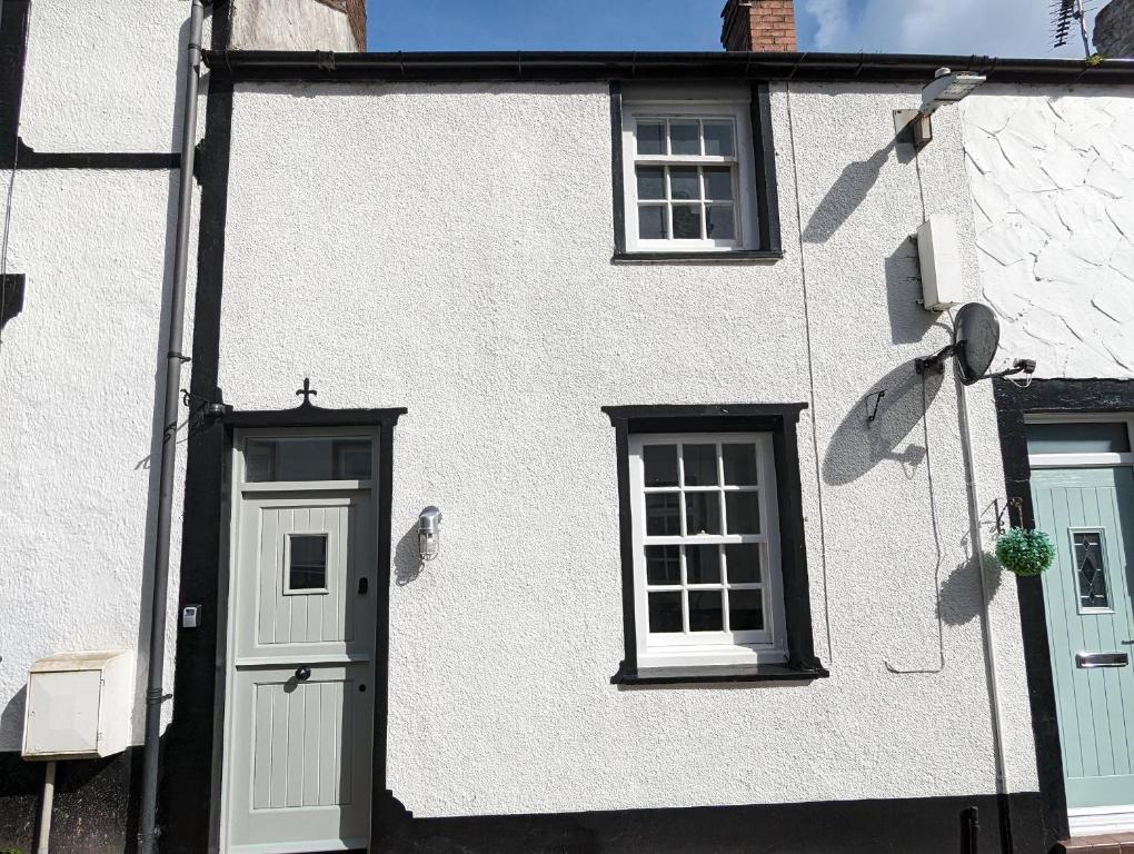 a white building with a door and two windows at Merywen Cottage in Conwy