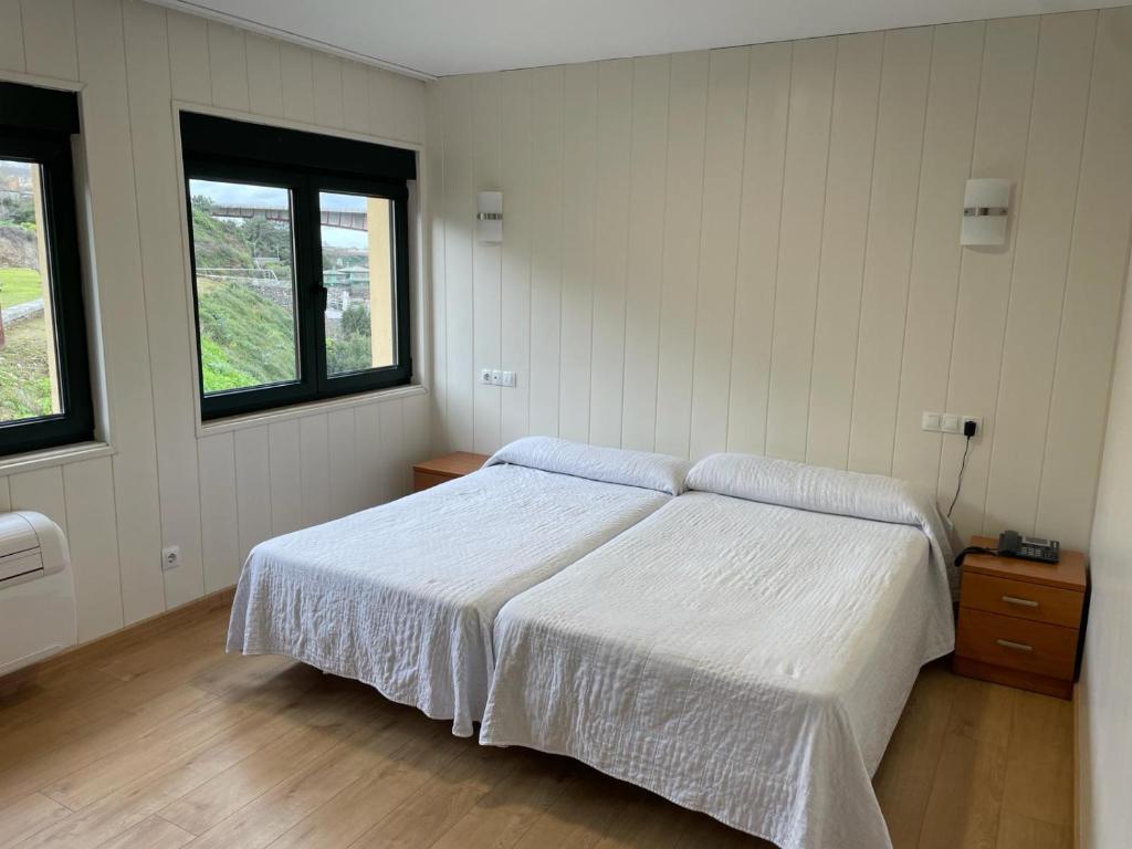 um quarto com uma cama branca e 2 janelas em Hotel Alda Fogar do Mariñeiro em Ribadeo