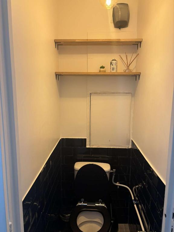 La salle de bains est pourvue de toilettes et d'un mur carrelé noir. dans l'établissement Appartement face stade de france, à Saint-Denis