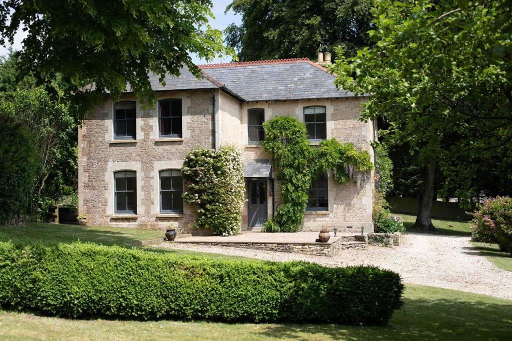 une ancienne maison en pierre avec des buissons devant elle dans l'établissement Trinity Farmhouse - Stunning House & Gardens!, à North Cerney