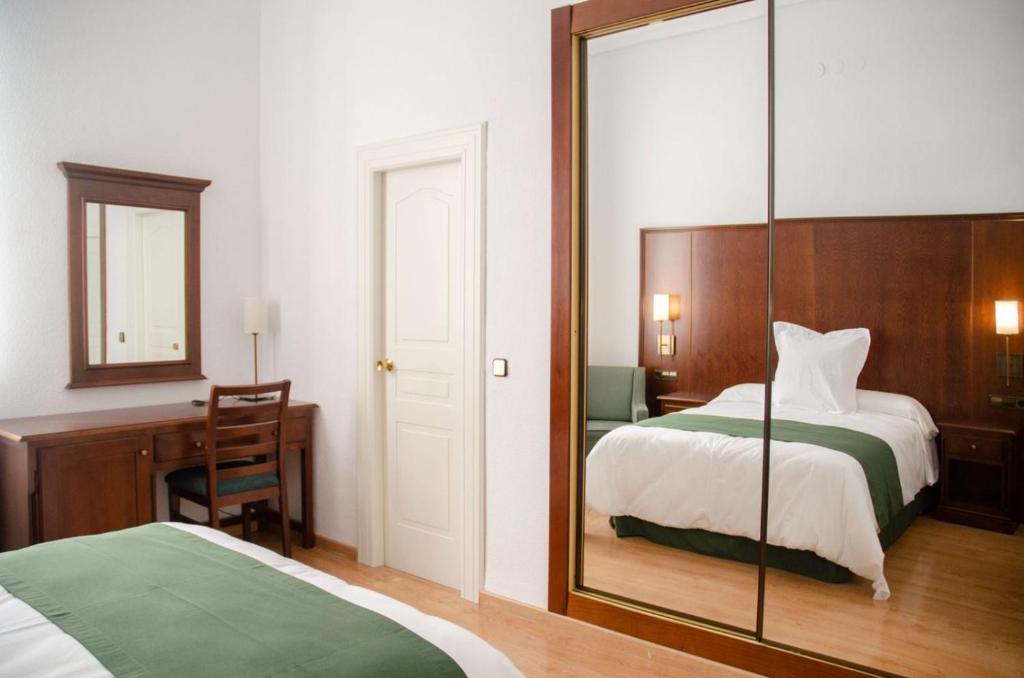 1 dormitorio con espejo, cama y escritorio en Hotel Balneario de Marmolejo, en Marmolejo