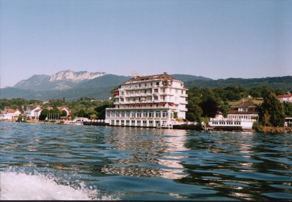a large building on the water with mountains in the background at Appartement Lumina in Maxilly-sur-Léman