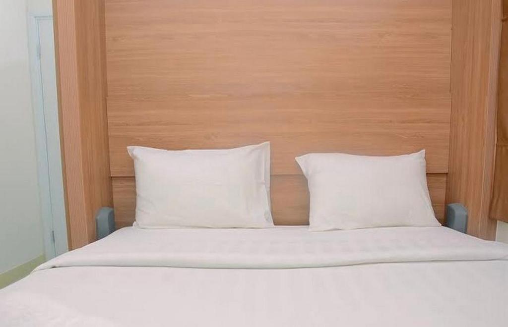 een bed met witte kussens en een houten hoofdeinde bij green pramuka city in Jakarta