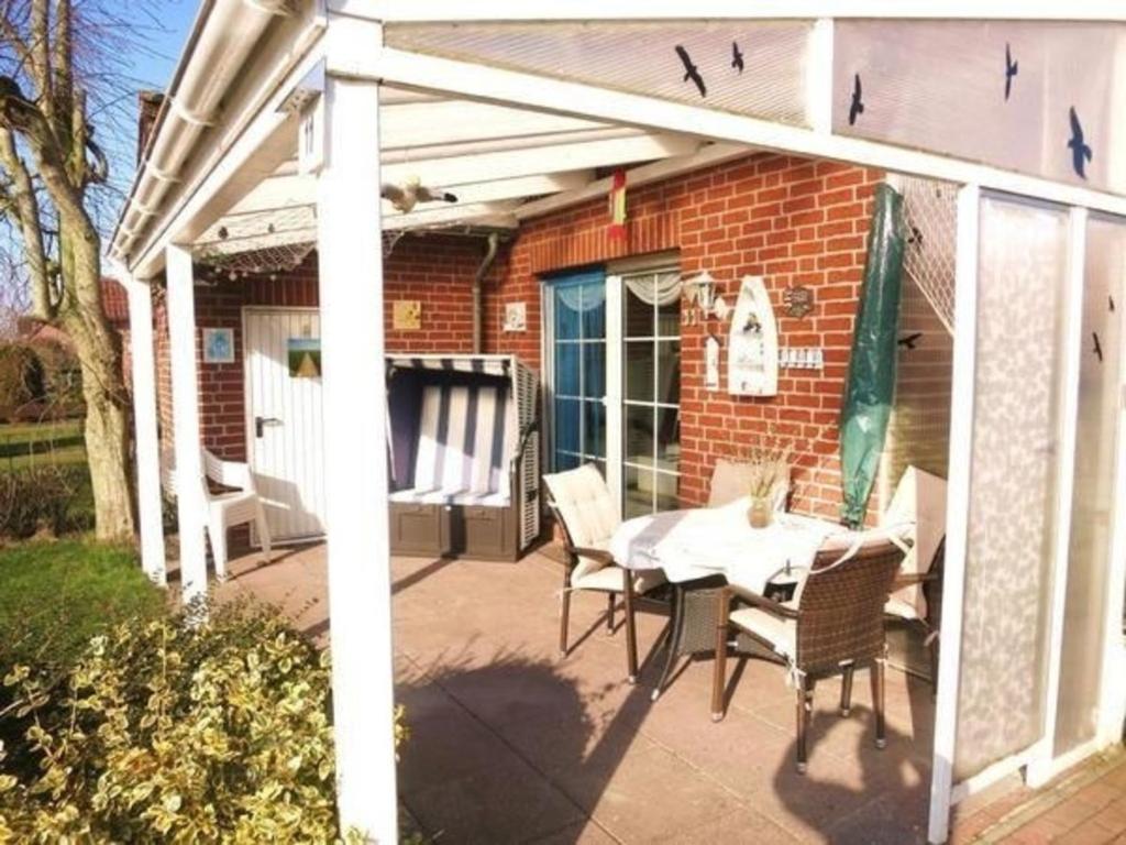 un patio avec une table et des chaises et un bâtiment dans l'établissement Ferienhaus Huus Wattenmeer in Nessmersiel mit Garten, Terrasse, Sauna, Räder, und Grill, à Dornum