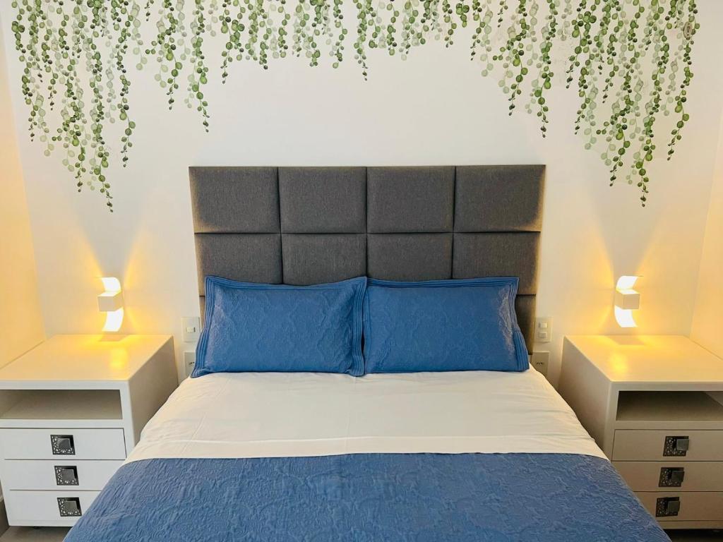 a bedroom with a bed with blue pillows and two lamps at Apartamento a 100 m da praia in Juquei