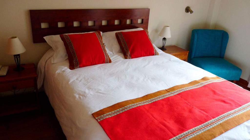 a bedroom with a bed with red pillows and a blue chair at Eco-Hotel Pension Alemana in Cusco