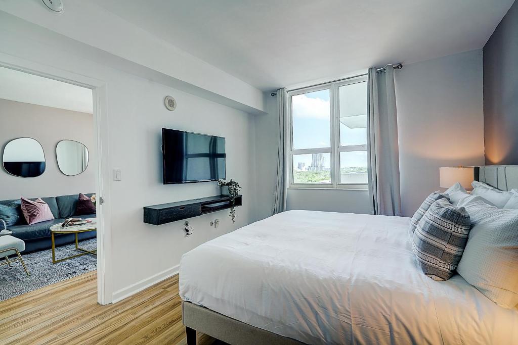 een witte slaapkamer met een bed en een televisie bij Coconut Grove 1 bedroom condo parking included in Miami