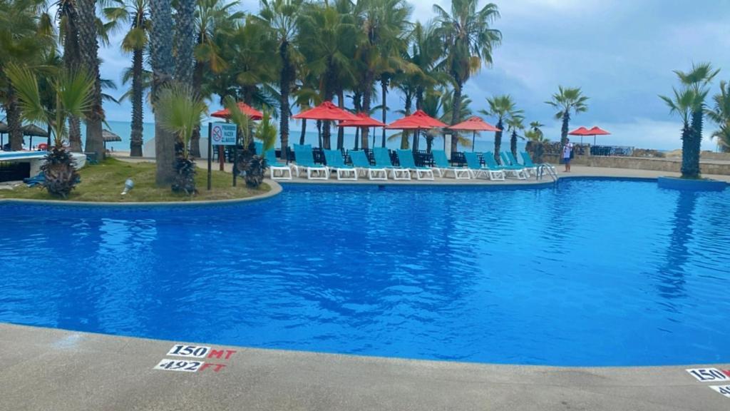 a large swimming pool with palm trees and red umbrellas at Punta Centinella Yacht Club in Santa Elena