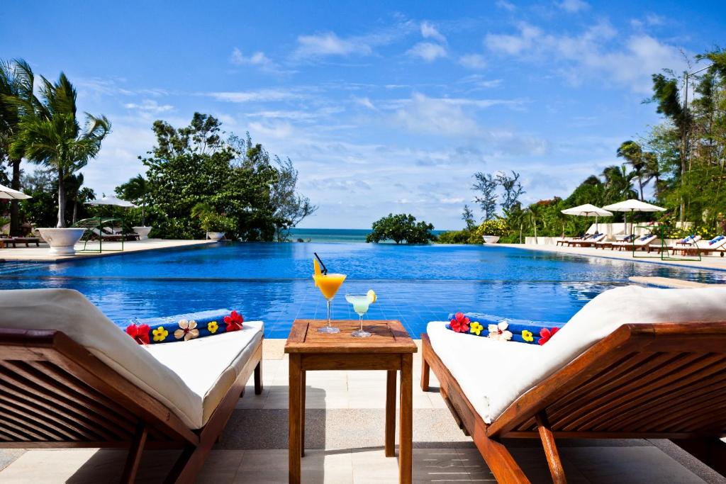 a pool at a resort with two chairs and a table at Victoria Phan Thiet Beach Resort & Spa in Mui Ne