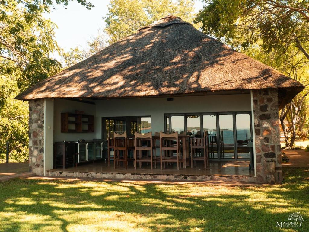 Binga的住宿－Masumu River Lodge，小屋设有茅草屋顶,配有桌椅