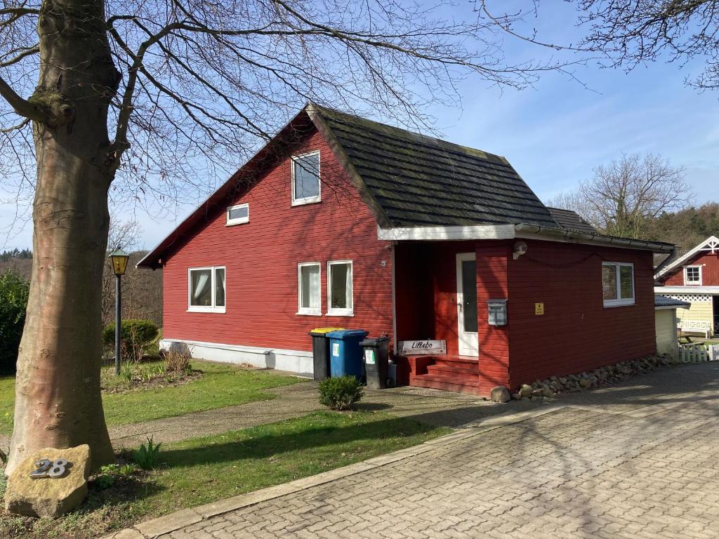 une maison rouge avec un arbre à côté d'une rue dans l'établissement Lillebo, à Lütjensee