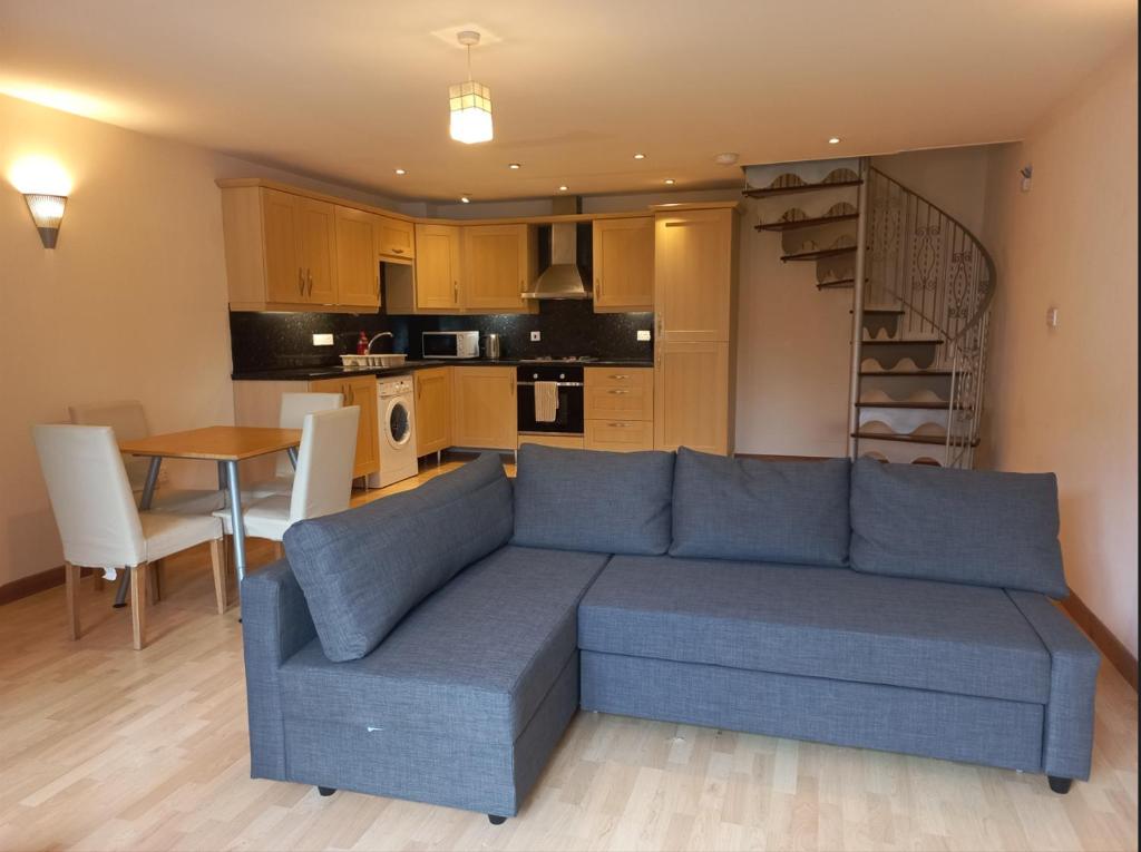 sala de estar con sofá azul y cocina en Maple Lodge, en Cheltenham
