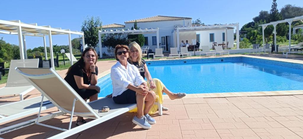 three women sitting on a bench next to a swimming pool at Hotel Baia Cea in Bari Sardo
