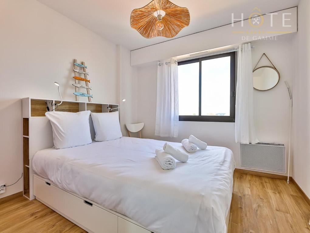 Un dormitorio blanco con una cama blanca grande con toallas. en Appartement au pied de la plage, vue imprenable sur la mer, en Les Sables-dʼOlonne