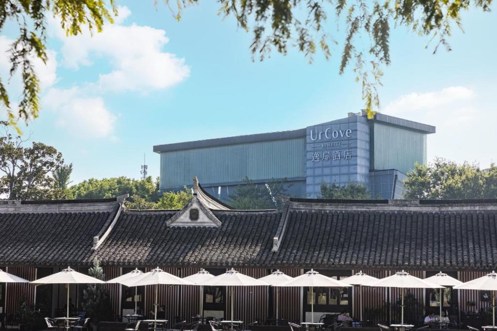 a building with tables and umbrellas in front of a building at UrCove by Hyatt Shanghai Pudong East in Shanghai