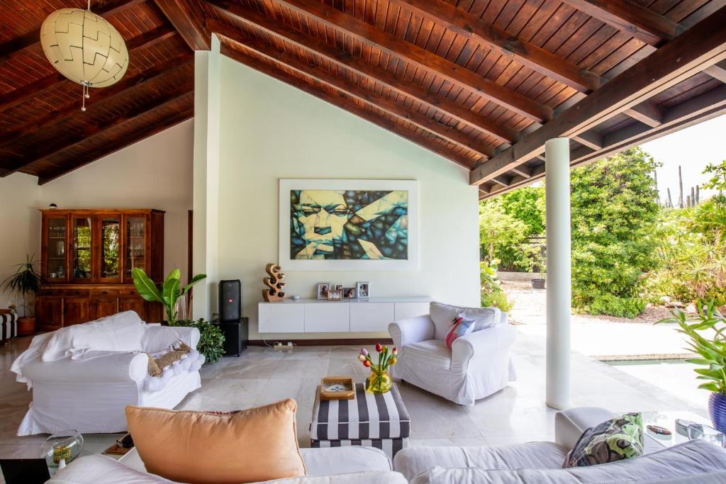 una sala de estar con muebles blancos y techo de madera. en Naïma Luxury Home, Cottage & Apartment Rentals, en Paradera