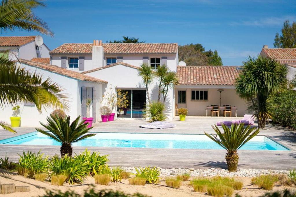 a villa with a swimming pool and palm trees at Maison au calme en lisière de forêt avec piscine chauffée in Ars-en-Ré