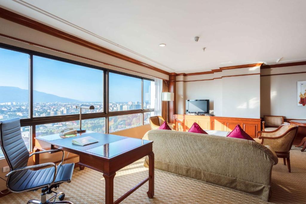 A living room includes a separate desk and office chair beside wide city-facing windows.