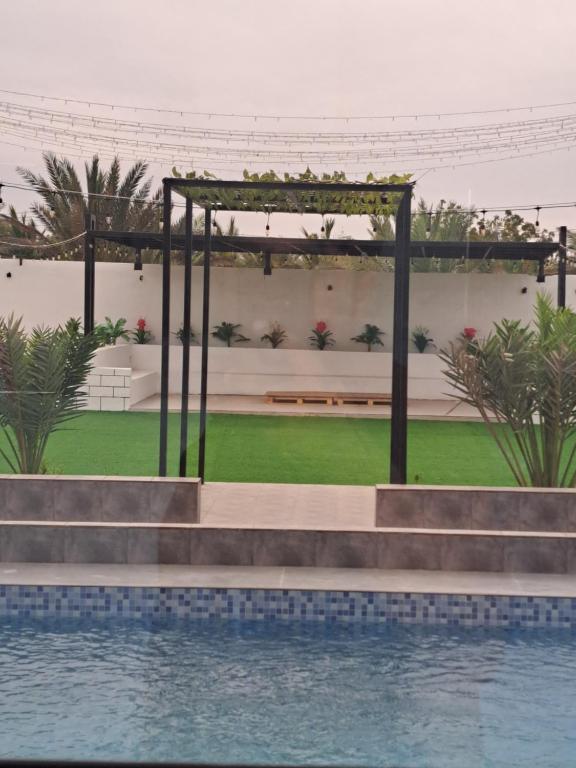 a pergola next to a pool with a bench at Gissah _farm in Ḩifrī