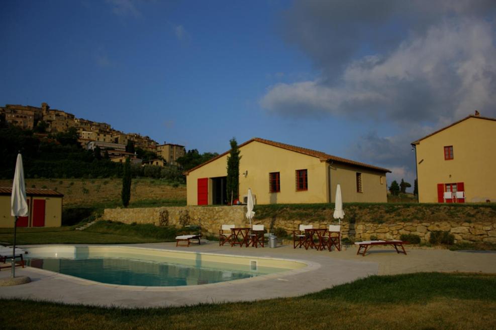 einen Pool mit Tischen und Stühlen und ein Gebäude in der Unterkunft Fattoria Podere i Luoghi in Casale Marittimo
