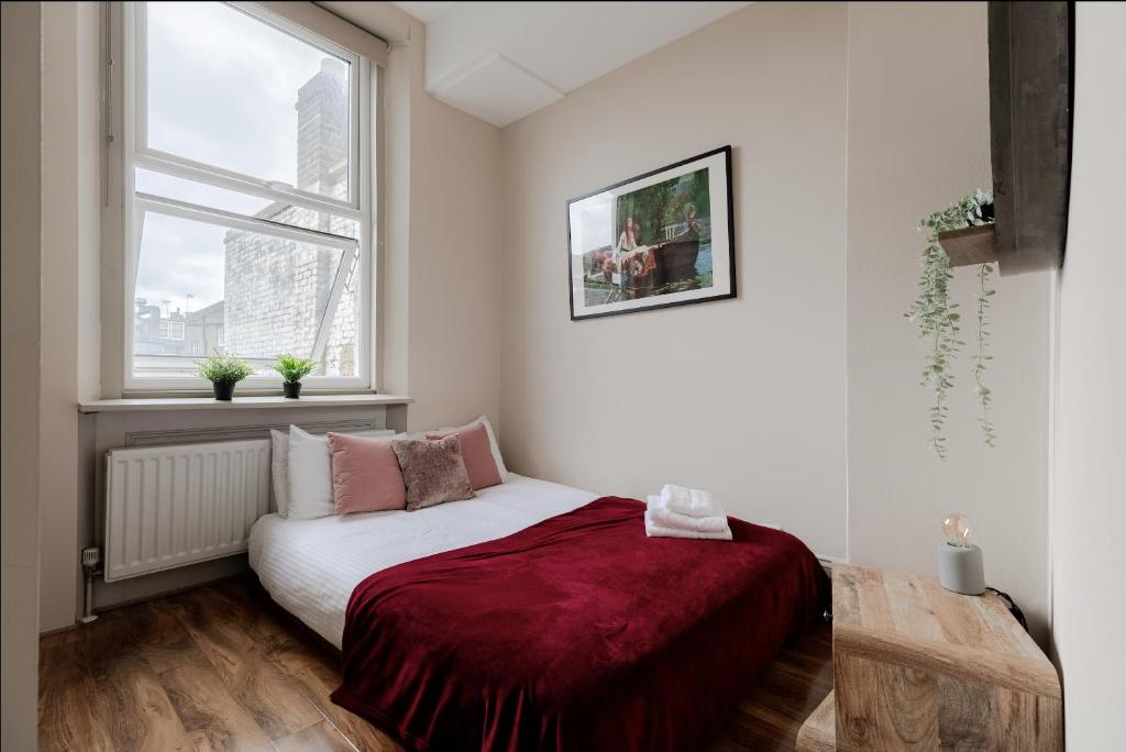 a bedroom with a bed with a red blanket and a window at Spacious & stylish 1-bed flat in Primrose Hill in London