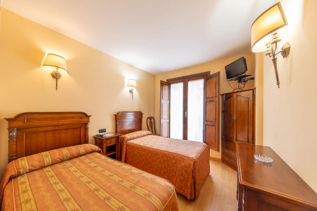 a hotel room with two beds and a desk at H-A Puerta de la Villa in Almazán