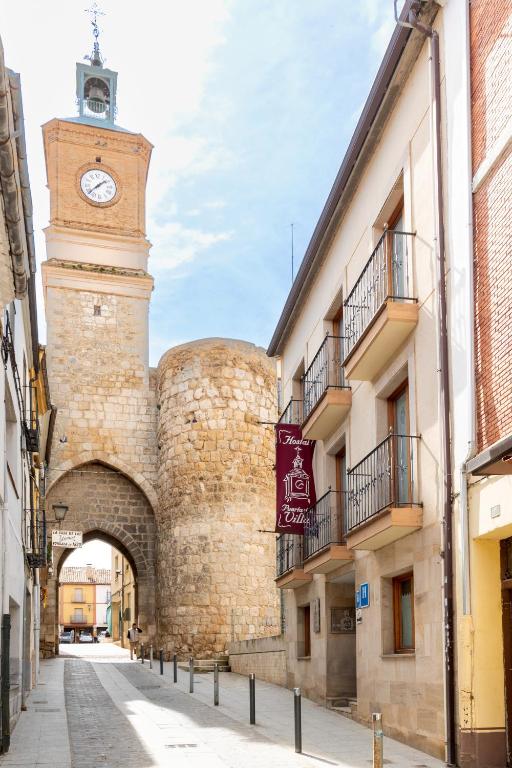 a building with a clock tower next to a street at Hostal SIN RECEP24H Puerta de la Villa - Pet friendly & Restaurante in Almazán