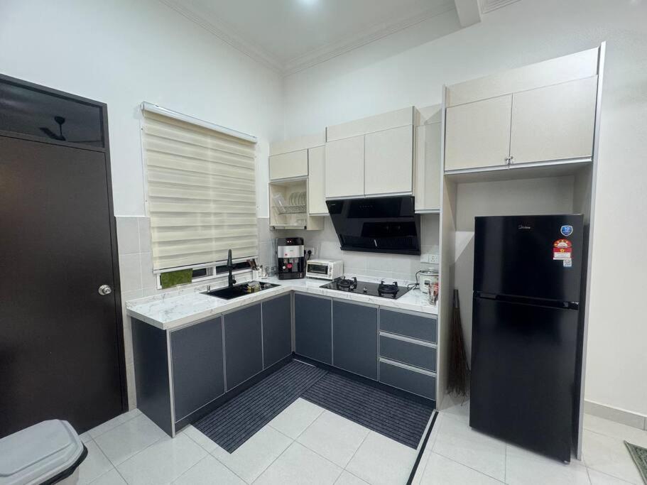 uma cozinha com um frigorífico preto e armários brancos em Hazzani Homestay KLIA em Banting