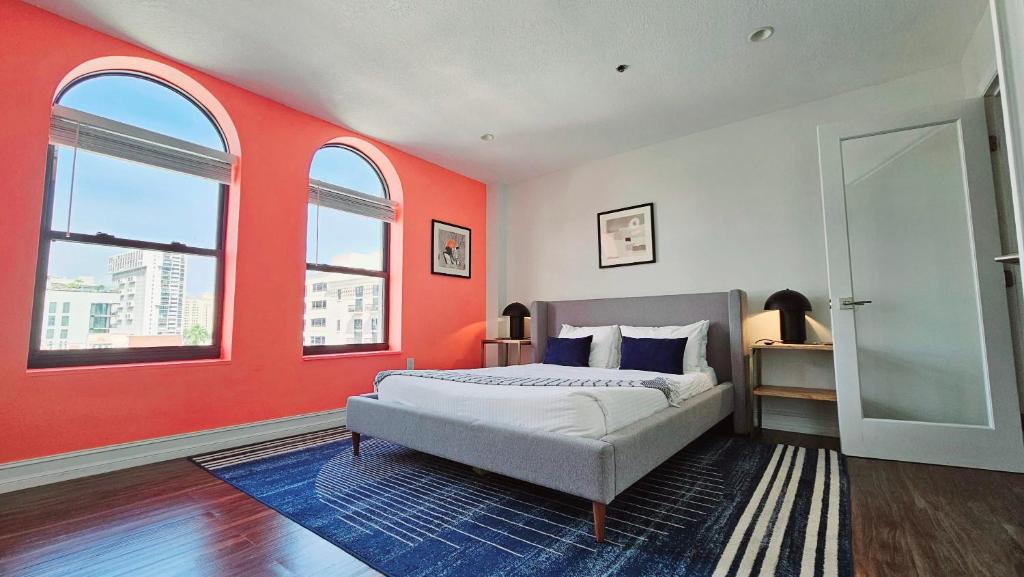 una camera da letto con una parete arancione, un letto e due finestre di The Lofts on Clematis 502 Downtown West Palm Beach a West Palm Beach
