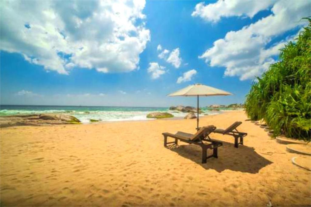 eine Bank am Strand mit einem Sonnenschirm in der Unterkunft Kamlo Beach Resort in Kirinda