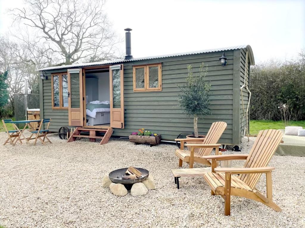 a green tiny house with chairs and a fire pit at Hidden Gem Luxury Shepherd Hut - Pea Pod in Wimbish
