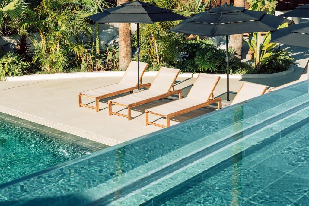 un gruppo di sedie e ombrelloni accanto alla piscina di Hotel Estefania Boutique Suites a Los Cristianos