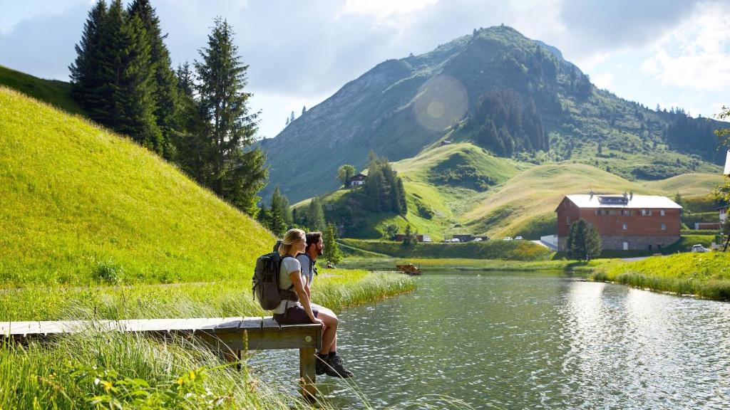 dwoje ludzi siedzących na moście nad rzeką z górą w obiekcie TOP 40 w mieście Warth am Arlberg