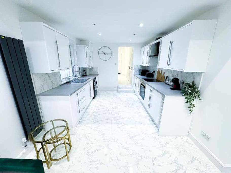 cocina con armarios blancos, mesa y silla en Modern Luxury 2 Bed with Parking, en Catford