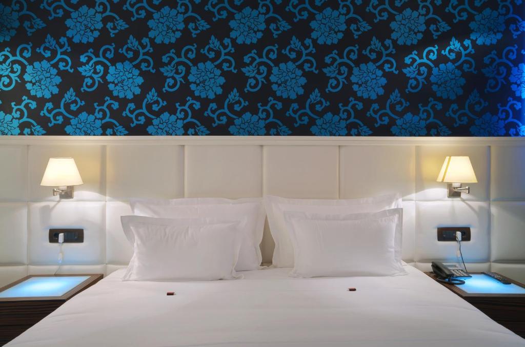 ein Schlafzimmer mit einem weißen Bett und einer blauen Tapete in der Unterkunft Garni Hotel Crystal in Kraljevo