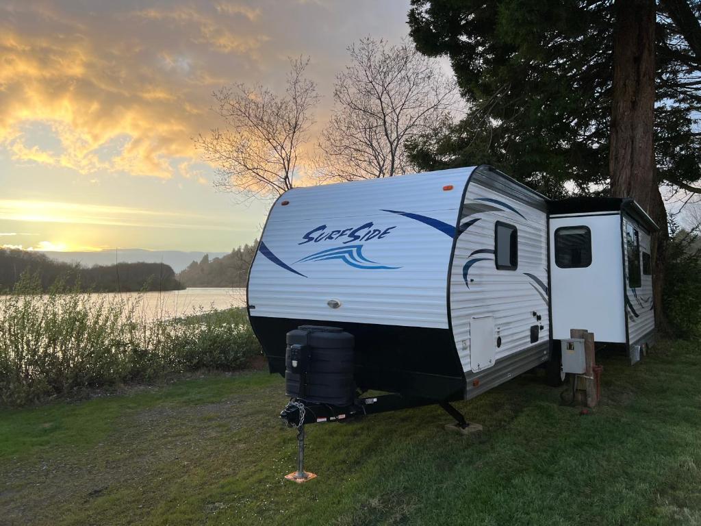a white trailer parked in the grass next to a lake at Surfside Glamping camper in Klamath