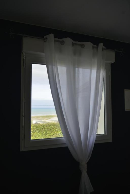 a window with a white curtain and a view of the ocean at Le Cottage de la Baie - vue mer en Baie de Somme in Woignarue