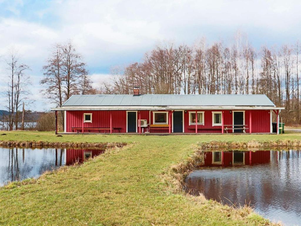 Holiday home VÅXTORP II في Våxtorp: منزل احمر على ارض فضاء بجانب سفح ماء
