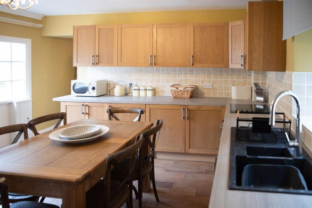 a kitchen with a wooden table and a kitchen counters at Gardeners Cottage in Longwitton