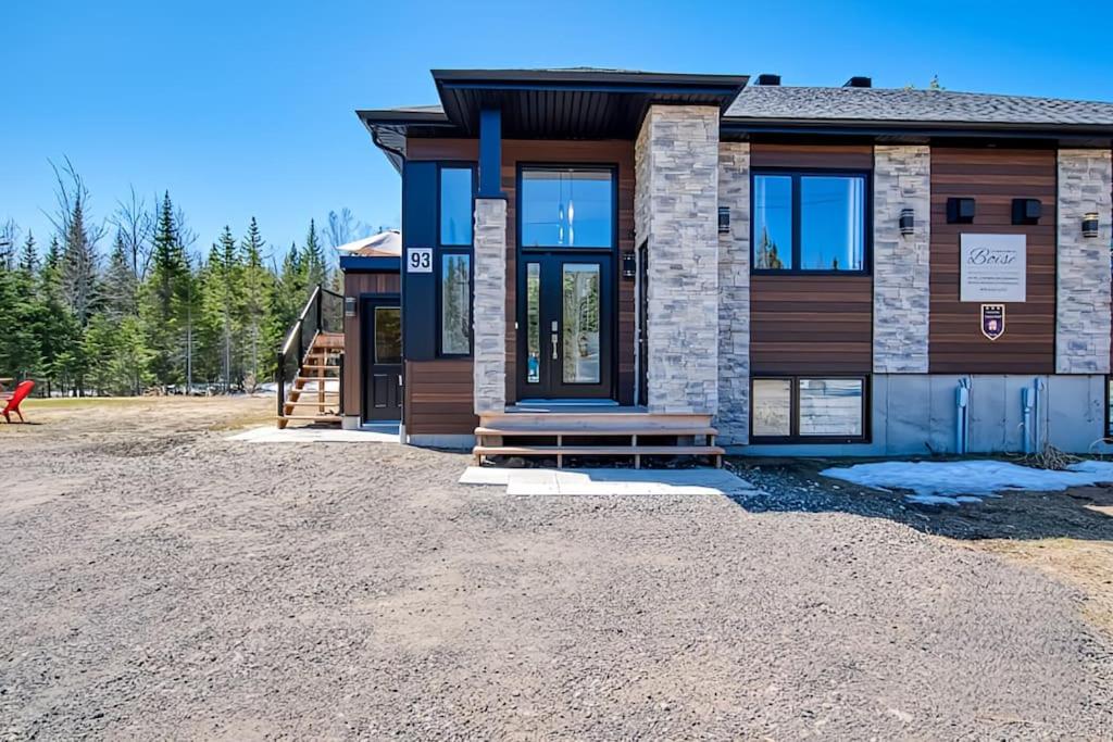 a house on a gravel lot with a building at Cottage Quebec - Olivine in Petite-Rivière-Saint-François