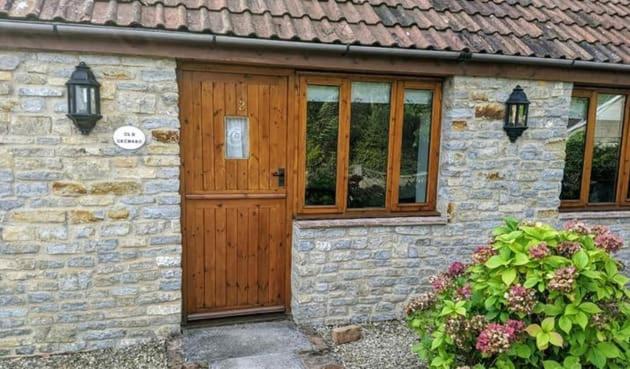 uma casa de pedra com uma porta de madeira e janelas em The Burcott Inn Cottages em Wells