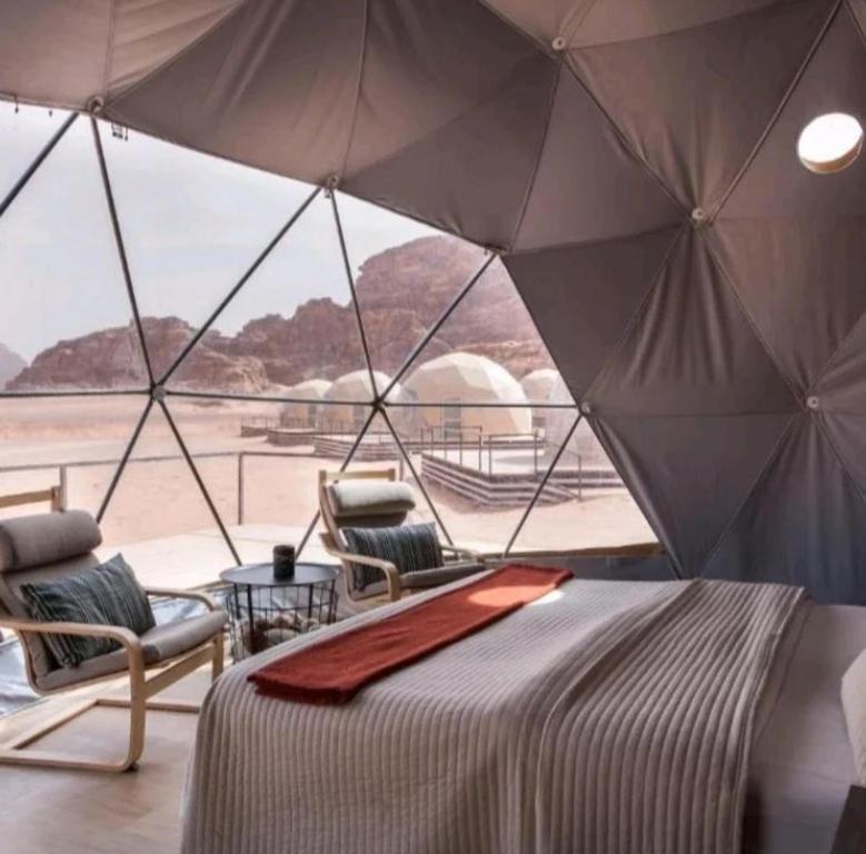 a bedroom with a bed and chairs and an umbrella at Rehana rum camp in Wadi Rum