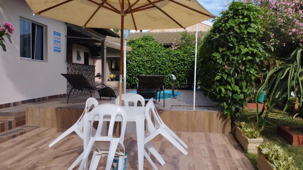 Duas cadeiras brancas e um guarda-sol num pátio em Casa c/ Piscina e Área Gourmet, 5 min da praia. em Guarapari