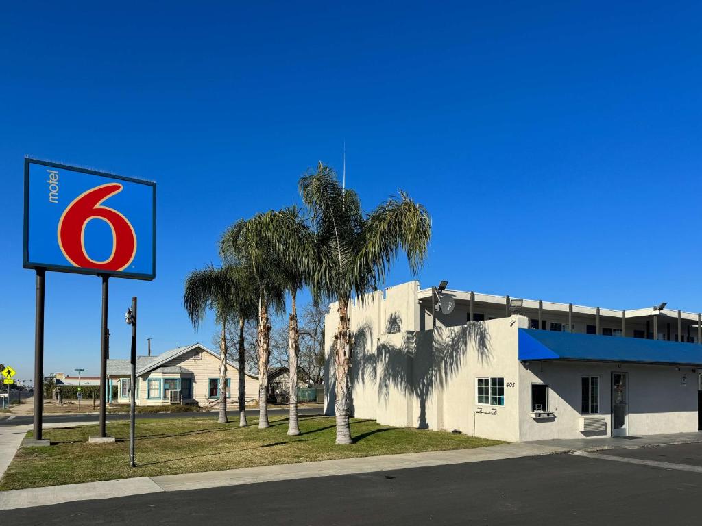 a sign in front of a building with palm trees at Motel 6-Delano, CA in Delano