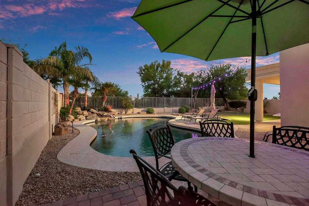 um pátio com uma mesa com um guarda-sol ao lado de uma piscina em Pool, Putting Green, Arcade, Cornhole, Great Location at Phoenix Desert Ridge Retreat! em Phoenix