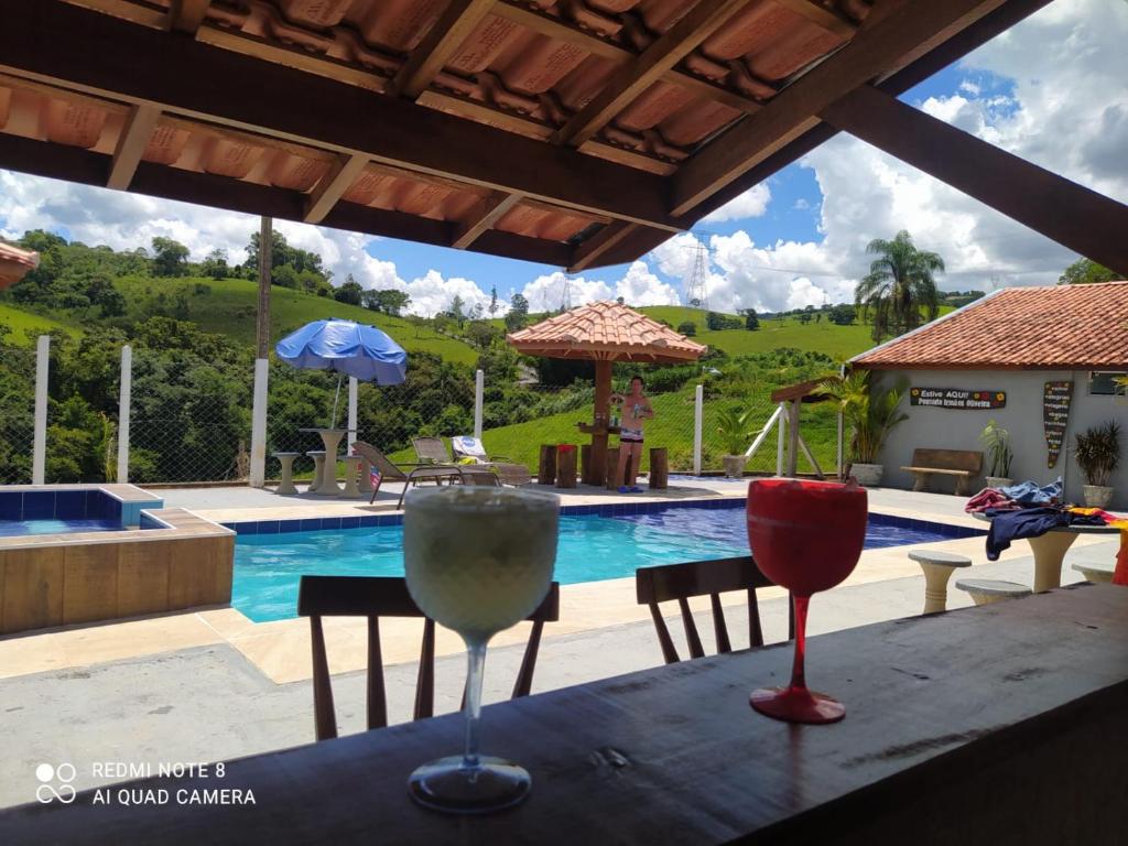 dos copas de vino sentadas en una mesa frente a una piscina en Pousada irmãos Oliveira en Lindóia