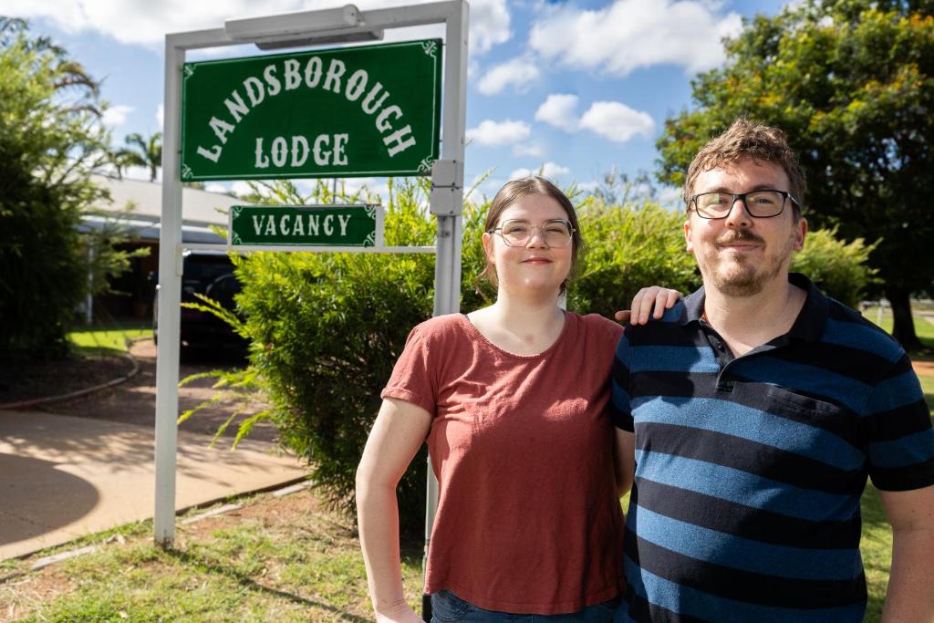 un hombre y una mujer parados frente a un letrero de la calle en Landsborough Lodge Motel, en Barcaldine